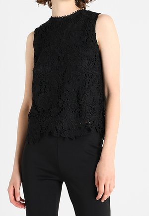 Mouwloze zwarte kanten top met bloemmotieven, gedragen met aangesloten zwarte broek, getoond op een staande persoon tegen een effen achtergrond.