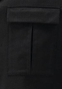 Black fabric featuring a flat pocket with a flap. Material has a smooth texture, and stitching is visible along the edges of the pocket.