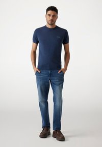 Camiseta navy de manga corta con cuello redondo y un logo, combinada con jeans de un azul claro y zapatos marrones de cordones. Textura de tela suave.