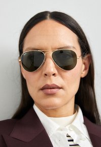 Ray-Ban aviator sunglasses with dark lenses, gold metal frame, double bridge design, and adjustable nose pads. Smooth finish and streamlined shape.