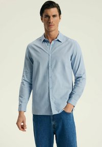 Jasnoniebieska koszula z długim rękawem na guziki z kołnierzykiem oraz subtelną teksturą, połączona z luźnymi niebieskimi dżinsami.
