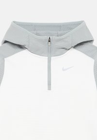 Svetlo šedá mikina s dlhým zipsom, bielym telom a štruktúrovanými šedými akcentmi. Má vysoký golier, krátky zips a malú šedú ikonu Nike na hrudi.