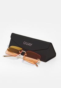 Ochelari de soare dreptunghiulari roșii și portocalii cu accente metalice aurii, așezați pe un etui triunghiular negru, embosat cu "QUAY". Lentile semi-transparente.