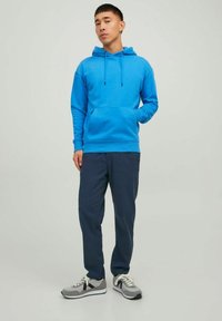 Blauwe katoenen hoodie met verstelbare koordjes en een voorkapsel, gecombineerd met donkerblauwe broeken en grijze sportschoenen.