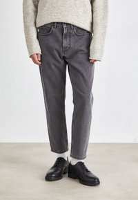 Jean en denim gris avec une coupe droite, taille moyenne et design classique à cinq poches, associés à des chaussures à lacets en cuir noir.