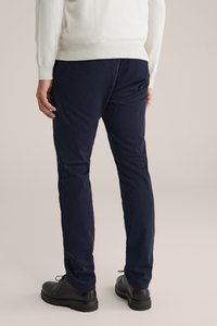 Mörkblå bomullbyxor med smal passform, slät textur och synliga sömmar. Bärs med svarta läderskor.