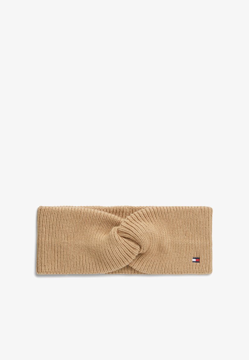 Bandeau beige en laine tricotée avec un centre torsadé et un petit écusson logo rectangulaire rouge, blanc et bleu sur un côté.