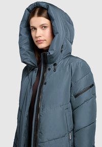 Steppjacke in Dunkelgrau mit großer Kapuze, Reißverschluss, Seitentaschen und einer strukturierten Oberfläche. Verfügt über schwarze Akzente und Nähte.