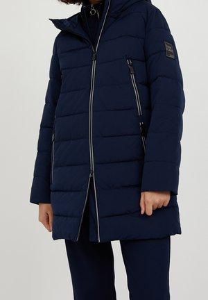Navy puffer jacket with horizontal quilting, front zipper, and removable hood. Features white accent piping and a logo patch on the sleeve.