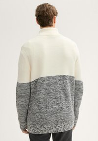 Gebreide pullover in crème en grijs, met een gestructureerde bovenkant en een patroon op de onderkant, voorzien van een hoge kraag en een losse pasvorm.