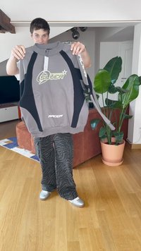 Felpa grigia con accenti neri, logo con la scritta "SILVER" e zip. Vestibilità ampia, abbinata a pantaloni neri a strisce zebrate e scarpe argento.