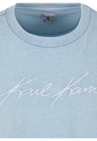 T-shirt en coton bleu clair avec un col rond et le texte brodé blanc "Karl" sur le devant, avec des détails de couture visibles.