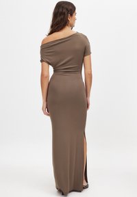 Lang, aansluitend jurk van bruine stof. Off-the-shoulder ontwerp met een zijsplit. Gladde textuur met minimale details.