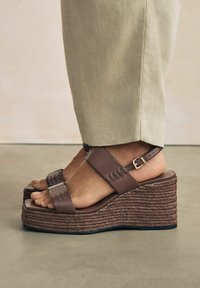 Brown wedge sandals with a braided jute sole, worn with light-colored pants, showcasing a relaxed, stylish summer look.