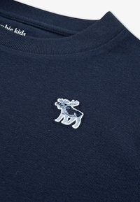 Pull en coton bleu marine avec un petit logo orignal brodé en bleu clair sur la poitrine gauche, col rond et texture douce.