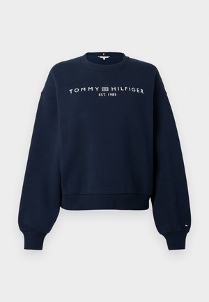 Temno modra majica z okroglim izrezom, z napisom „Tommy Hilfiger EST. 1985“ v belih črkah na prsih, z rebrastimi manšetami in spodnjim robom.