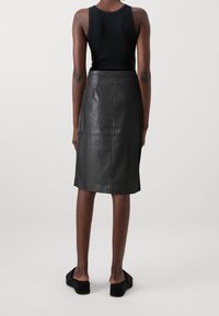 Zwarte leren kokerrok met een middelhoge taille en stikdetails, gecombineerd met een zwarte mouwloze top en zwarte platform sandalen.