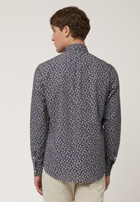 Langsleeve overhemd van marineblauw stof met een klein bloemmotief in geel en wit, met een standaard kraag en een gebogen zoom.