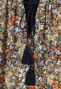 Tissu à motif floral avec des fleurs bleu marine, orange et jaune. Comprend un lien de cou avec deux pompons noirs, léger et texturé.