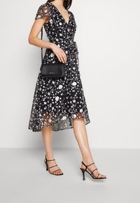 Černé květinové šaty s krátkými, průhlednými rukávy, výstřihem do V a páskem na zavázání v pase. V kombinaci s černými sandály na podpatku a malou černou kabelkou.