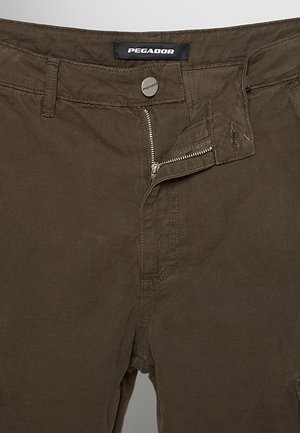 Pantaloni marroni con cerniera metallica parzialmente aperta, bottone marchiato ed etichetta "Pegador" in vita.