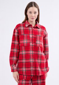 Czerwona koszula w kratę z flaneli, z długimi rękawami, zapinana na guziki z dwoma naszytymi kieszeniami i kołnierzykiem w szpic. Miękka tekstura i luźny krój.