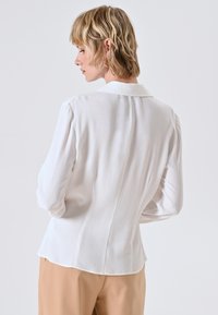 Witte blouse met een kraag, lange mouwen en een zachte textuur. Heeft voor- en achterpanden voor een getailleerde pasvorm en een subtiele glans.