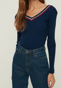 Haut bleu marine à manches longues côtelées avec un décolleté en V agrémenté d'accents rayés rouges et blancs, associé à un jean en denim foncé taille haute.