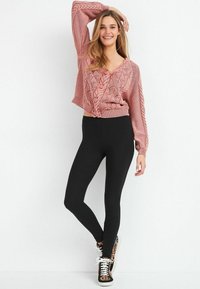 Lichtroze cropped sweater met kabelbrei-design, gecombineerd met zwarte leggings en sneakers met luipaardprint, met een relaxte pasvorm en V-hals.