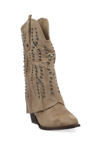 Botín beige de ante con punta afilada, adornado con tachuelas plateadas en un patrón ondulado, y un tacón bajo apilado. Diseño con recortes.