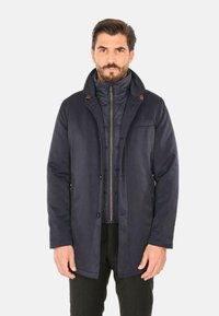 Cappotto blu navy con collo, dotato di uno strato interno con zip e dettagli marroni. Realizzato in tessuto liscio, ha un design aderente e tasche.