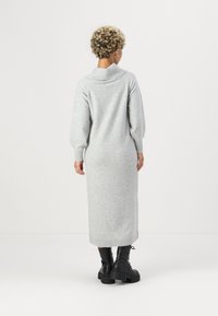 Vestido em malha cinza claro, com gola alta, mangas longas e punhos canelados. Combinado com botas pretas de plataforma grossa.