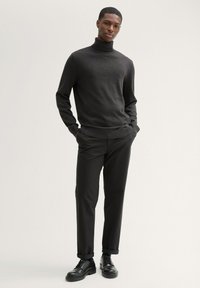 Czarny sweter o wysokim kołnierzu w miękkiej fakturze, zestawiony z dopasowanymi czarnymi spodniami i czarnymi sznurowanymi butami. Prosty, nowoczesny design.