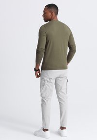 Olivgrünes Langarmshirt mit Rundhalsausschnitt, kombiniert mit hellgrauen Cargo-Hosen mit Seitentaschen und elastischen Bündchen, getragen mit weißen Sneakers.