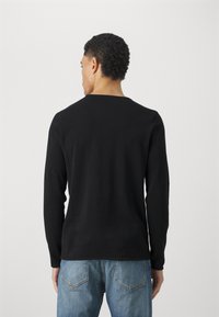 Cămașă neagră cu mânecă lungă și guler rotund, realizată dintr-un material moale, având o siluetă ajustată și un design minimalist. Purtați-o cu blugi albaștri.