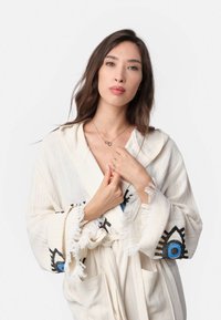 Krémová róba s strapcami, so čiernymi a modrými vyšívanými akcentmi na rukávoch. Mäkká textúra a otvorený predný dizajn.