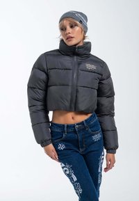 Puffige, cropped schwarze Jacke mit hohem Kragen und Reißverschluss. Kombiniert mit blauen Jeans aus Denim mit weißen gestickten Designs.