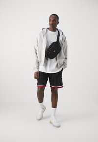 Pantaloni neri con accenti rossi, t-shirt bianca, felpa oversize grigia chiara e borsa a tracolla nera. Sneakers bianche con accenti colorati.