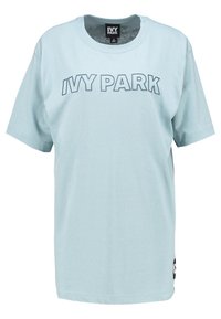 Camiseta de algodón en color azul claro, de corte oversize, con el texto "IVY PARK" en un tono de azul más oscuro, mangas cortas y una etiqueta en el lado inferior.
