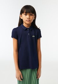 Navyblauw poloshirt met korte pofmouwen en kraag, voorzien van een klein groen krokodillogo op de borst. Materiaal lijkt zacht en gestructureerd.