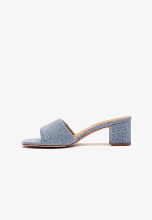 Mule open-toe in denim azzurro chiaro con cinturino largo e tacco largo di media altezza, mostrata di profilo su sfondo bianco.