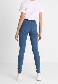 Jeans skinny in denim, con design a vita alta, dotati di due tasche posteriori e una superficie liscia. Abbinati a una maglietta rosa chiaro.