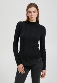 Zwarte geribde gebreide turtleneck trui met lange mouwen en een aansluitende zoom. Gecombineerd met verticale textuur lijnen voor een gestructureerde uitstraling.