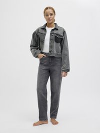 Siva denim jakna z gumbom na sprednji strani in sprednjimi žepi, v kombinaciji s sivimi visokotlaščenimi jeansom. Model ima bose noge in ravne lase.