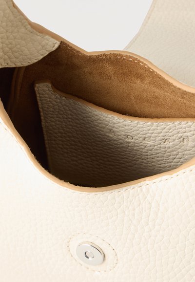 Εκμαγείο ενός ανοιχτού δερμάτινου τσάντας σε κρεμ απόχρωση με υφή, που δείχνει το σουέντ εσωτερικό και το μαγνητικό κουμπί κλεισίματος.