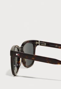 Lunettes de soleil en écaille de tortue avec verres gris. Elles présentent une forme rectangulaire et un accent logo en métal argenté sur la branche. Fabriquées en matériau plastique.