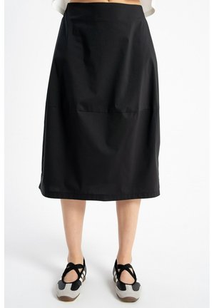 Czarna spódnica midi noszona z czarno-białymi sneakersami z krzyżującymi się paskami na białym tle.