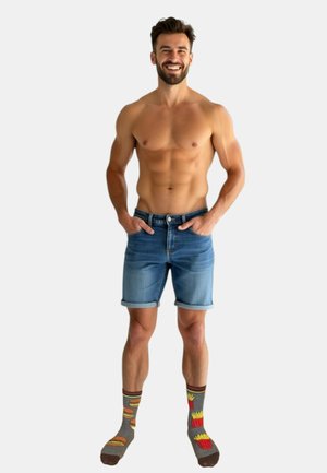 Denim shorts met opgerolde boorden, lichtblauwe kleur. Dikke gebreide sokken met een patroon van hamburgers en frietjes. Model is bloot bovenlijf, glimlachend.