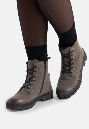 Szare skórzane botki za kostkę z przodem na sznurowadła, bocznym zamkiem błyskawicznym i teksturowaną gumową podeszwą. Nad butem widoczne czarne, prążkowane skarpetki.