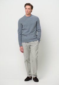 Hellblaues Strickoberteil mit Rundhalsausschnitt, kombiniert mit hellgrauen Hosen. Braune Schuhe runden den Look ab und schaffen ein modernes Outfit.